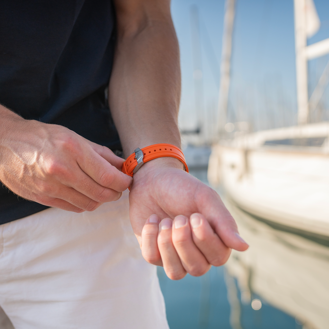 Person adjusting an orange watch on a boat with water and sky in the background