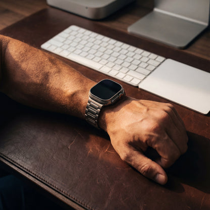 Person's wrist with a smartwatch on a desk with a computer setup