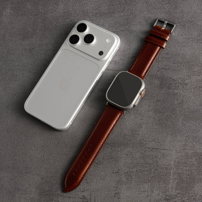 A silver smartphone and a smartwatch with a brown leather strap, arranged diagonally on a textured gray surface.