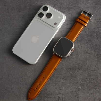 A silver smartphone and a smartwatch with a tan leather strap are arranged diagonally on a textured dark gray surface.