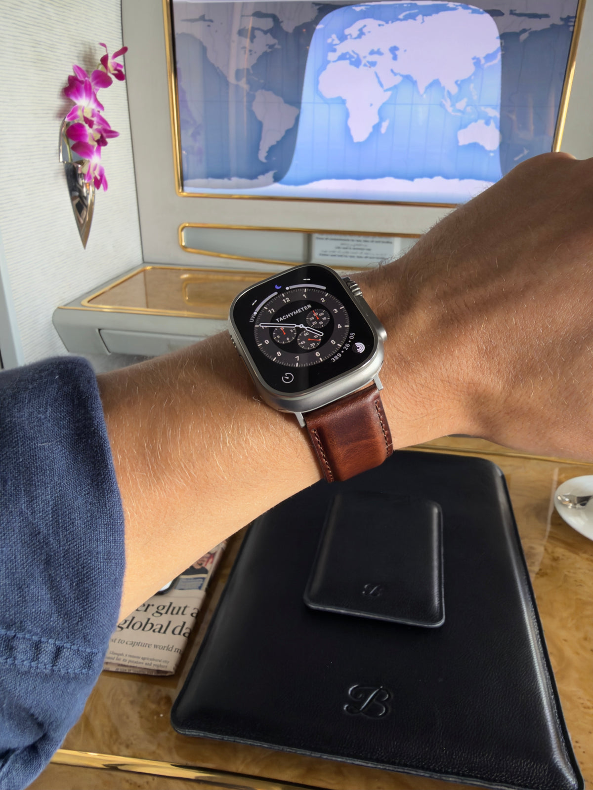 The Heritage dark brown leather strap on an Apple Watch Ultra, worn with a navy shirt while travelling