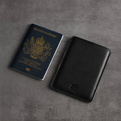 Black leather passport sleeve next to a British passport, angled close-up – The Bridge
