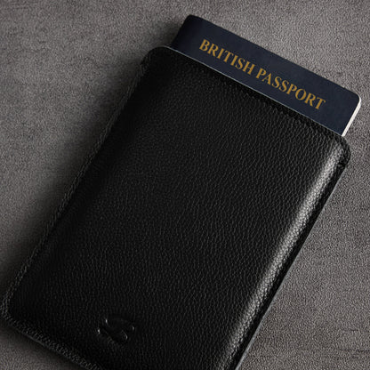 Black leather passport sleeve with British passport partially inserted, angled view – The Bridge