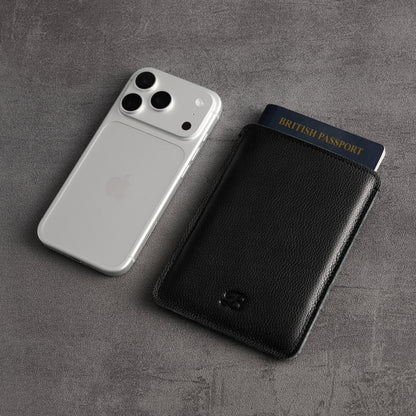 Black leather passport sleeve and British passport next to silver iPhone – The Bridge