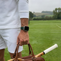 Person holding a brown leather duffel bag with an apple watch strap.