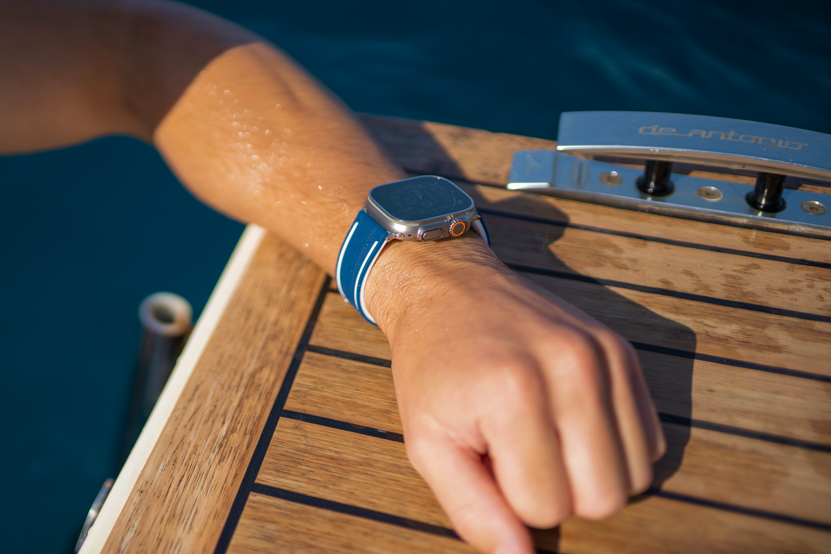 Wrist with a blue Apple Watch strap resting on the teak deck of a boat