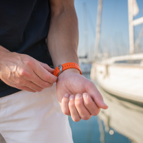 Person adjusting an orange watch on a boat with water and sky in the background