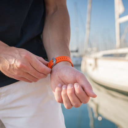 Person adjusting an orange watch on a boat with water and sky in the background