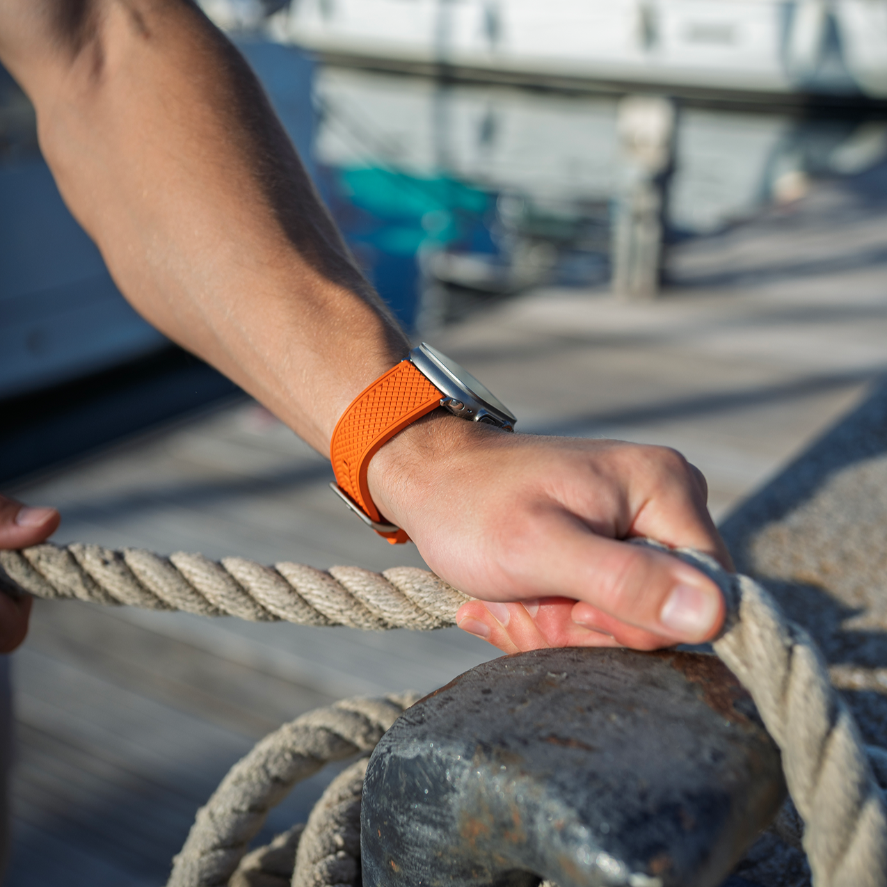 Hand holding a rope tied to a cleat with a marina background