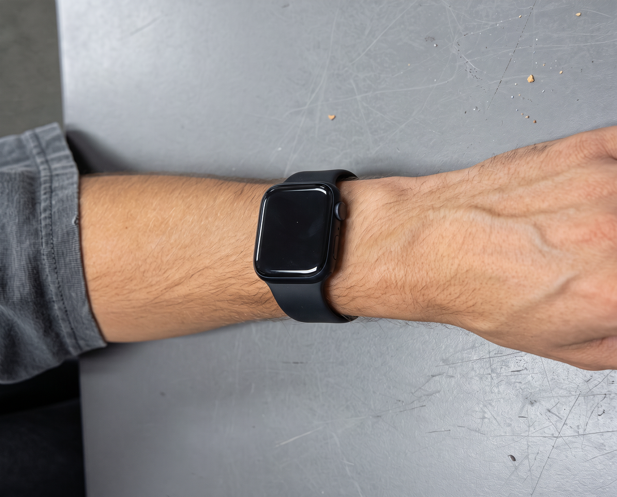 Man's wrist wearing an Apple Watch on a plain black sport band, resting on a grey office desk